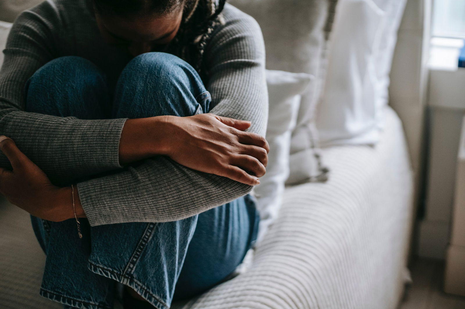 woman sitting on bed hugging her knees