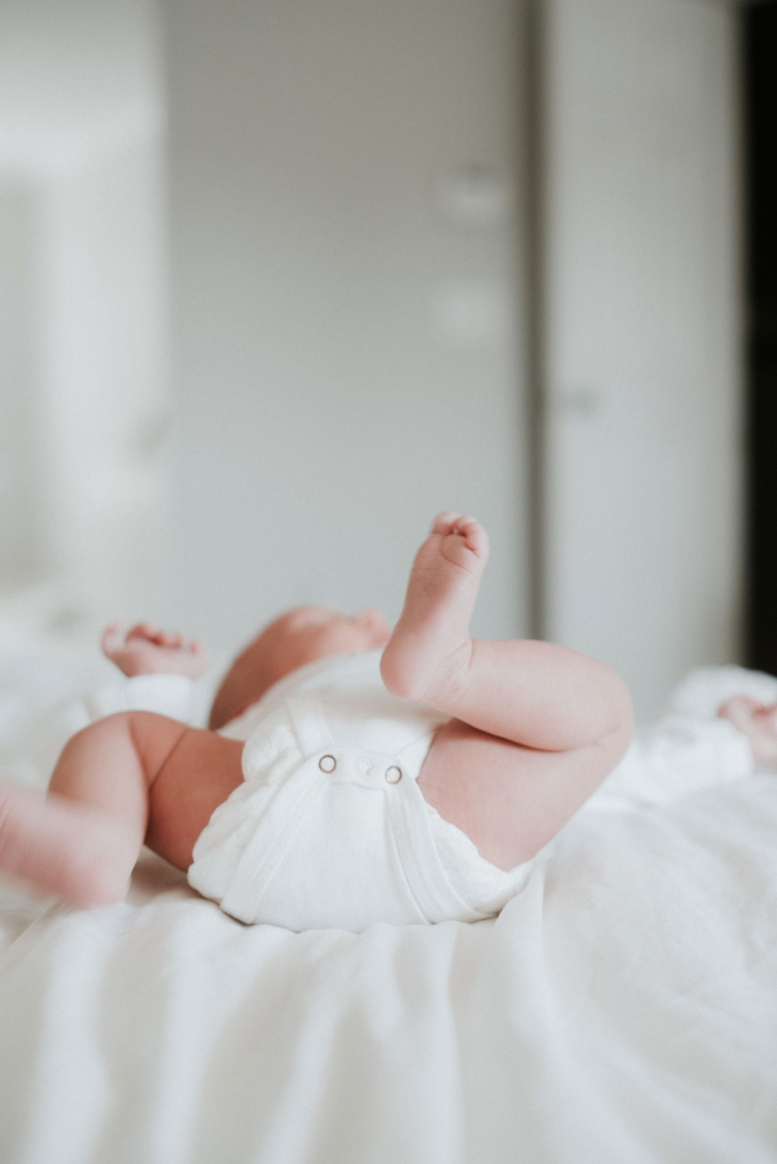 Pale skinned baby lying on their back on a bed, wearing a diaper. View from the feet.