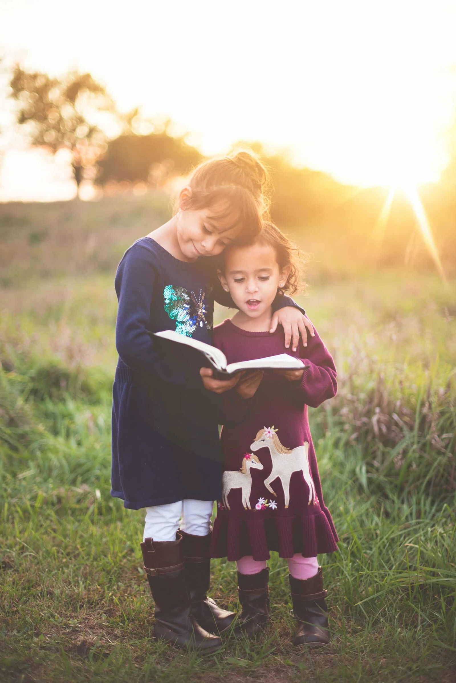 two girls reading a book together in the sunlight 