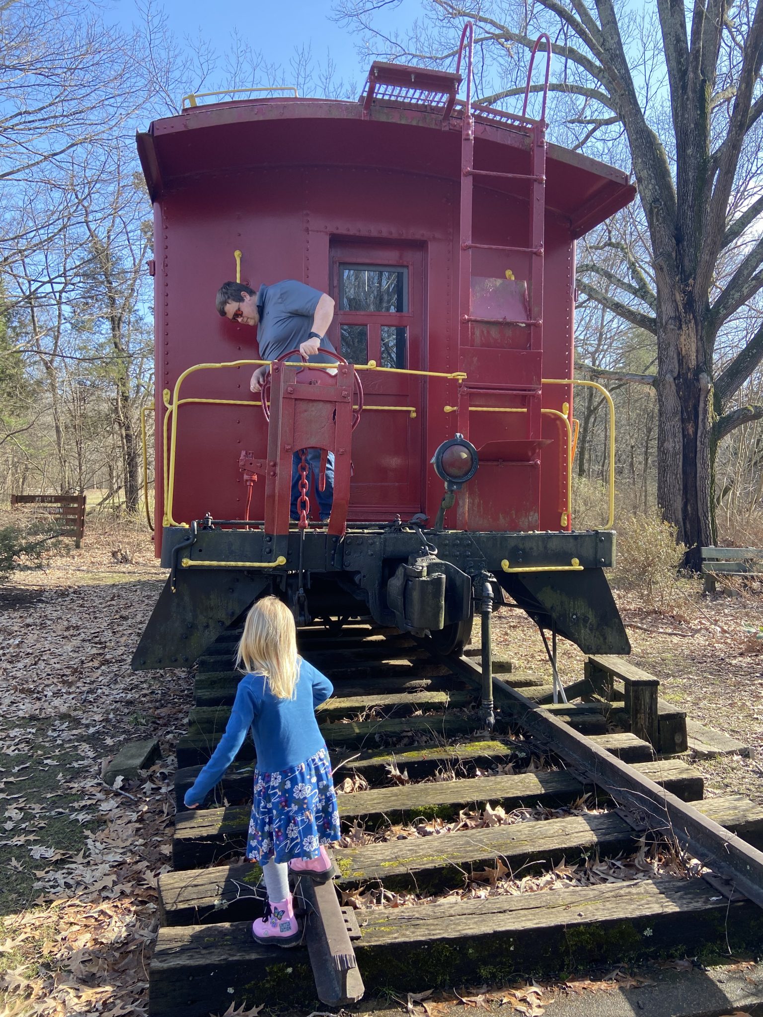 man on front of a red train on a train track with a little girl running to him on the train track