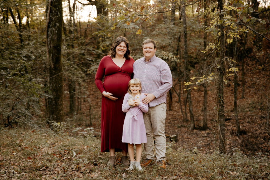 Pregnant woman, husband and little girl with stuffed birds standing in the forest